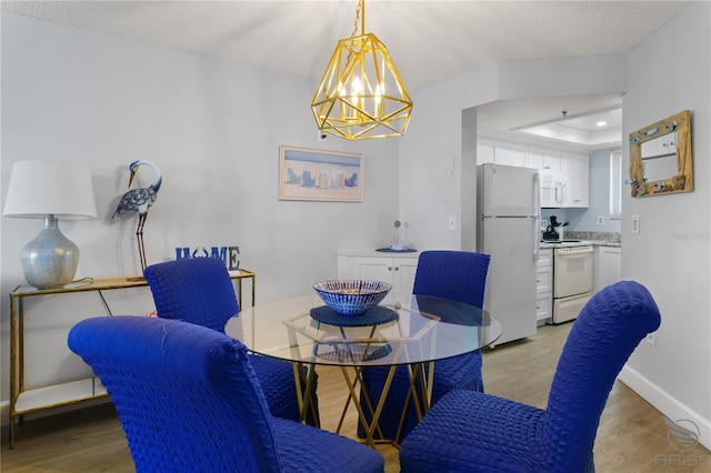 dining space featuring a tray ceiling, light hardwood / wood-style floors, a textured ceiling, and a notable chandelier