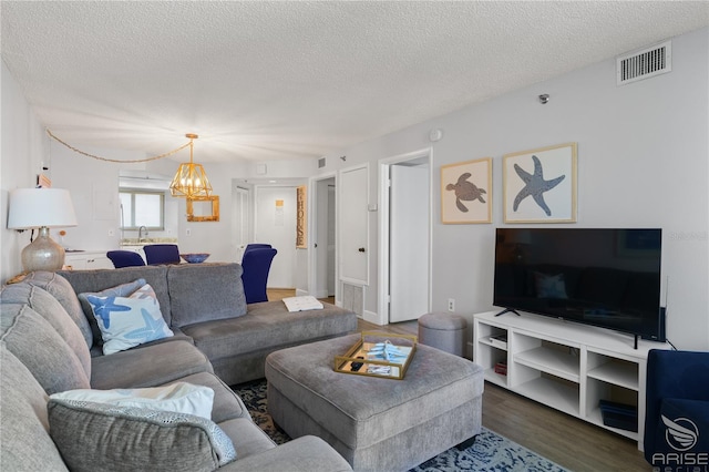 living room with hardwood / wood-style flooring, a chandelier, sink, and a textured ceiling