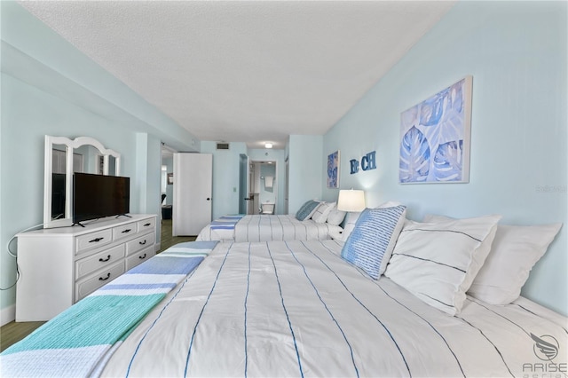 bedroom featuring connected bathroom, hardwood / wood-style flooring, and a textured ceiling