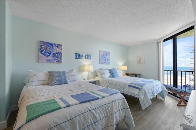 bedroom featuring floor to ceiling windows, a water view, a textured ceiling, hardwood / wood-style flooring, and access to exterior