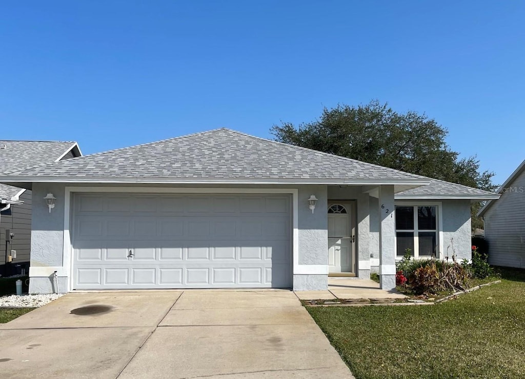 ranch-style home with roof with shingles, an attached garage, and stucco siding