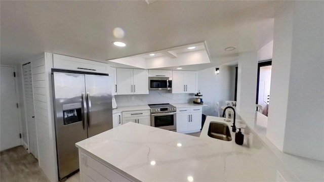 kitchen with white cabinetry, sink, light stone counters, kitchen peninsula, and stainless steel appliances