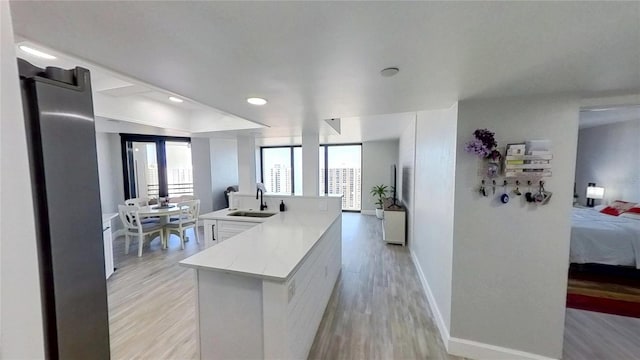 kitchen featuring white cabinetry, sink, an island with sink, and light wood-type flooring