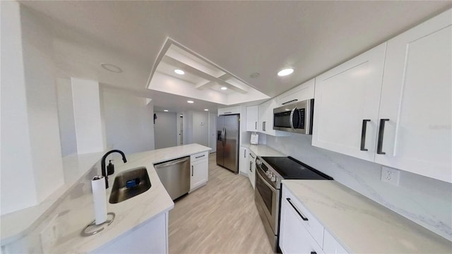 kitchen with sink, white cabinetry, light stone counters, light hardwood / wood-style flooring, and appliances with stainless steel finishes