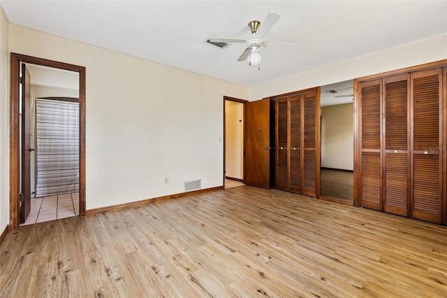 unfurnished bedroom featuring two closets, light hardwood / wood-style flooring, ensuite bath, and ceiling fan