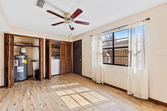 unfurnished bedroom featuring washer and dryer, light hardwood / wood-style flooring, water heater, and multiple closets