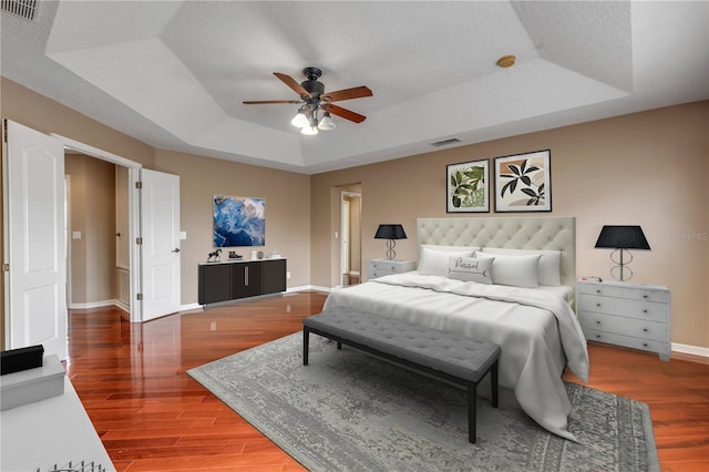 bedroom with a raised ceiling, hardwood / wood-style floors, a textured ceiling, and ceiling fan