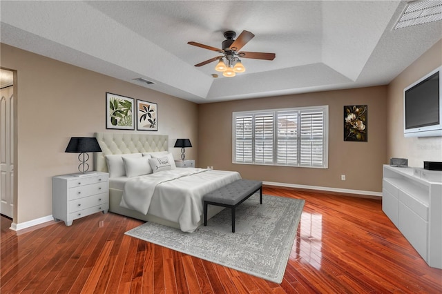 bedroom with a raised ceiling, wood-type flooring, ceiling fan, and a textured ceiling