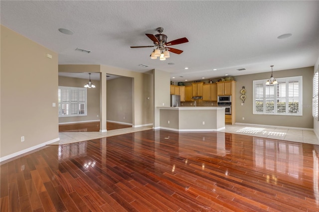 unfurnished living room featuring ceiling fan with notable chandelier, a textured ceiling, and light hardwood / wood-style flooring