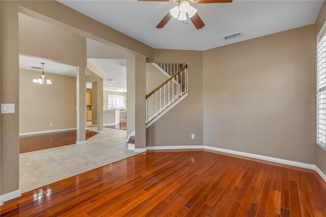 unfurnished room with ceiling fan with notable chandelier and light hardwood / wood-style flooring