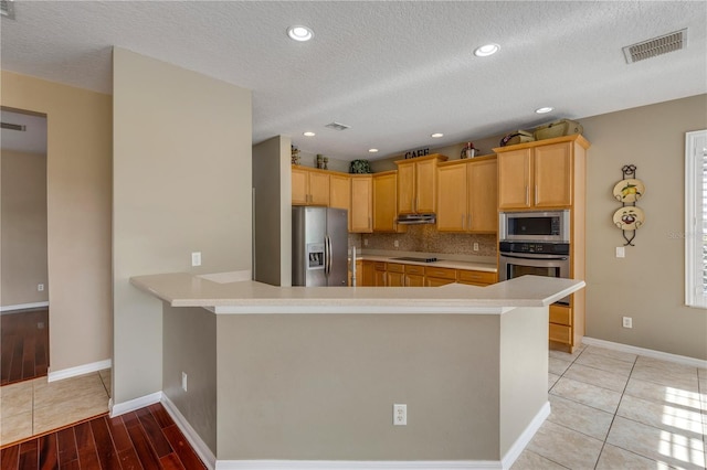 kitchen featuring light tile patterned floors, backsplash, stainless steel appliances, light brown cabinetry, and kitchen peninsula