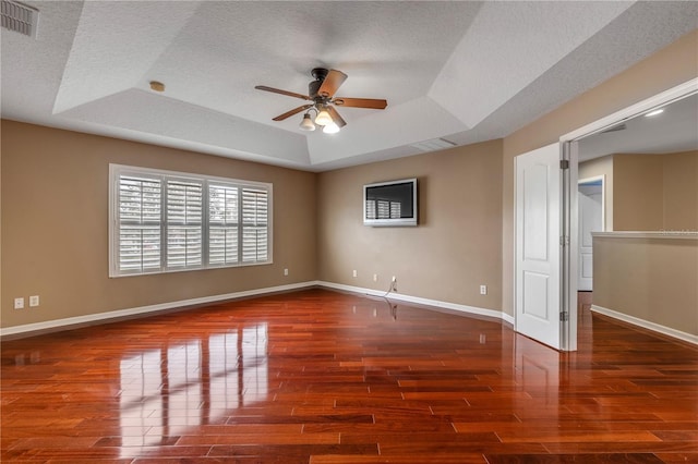 unfurnished room with dark wood-type flooring, ceiling fan, a tray ceiling, and a textured ceiling