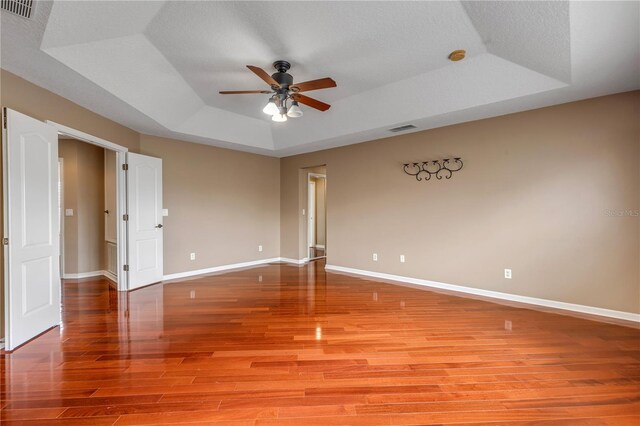 spare room with a textured ceiling, a raised ceiling, ceiling fan, and light wood-type flooring