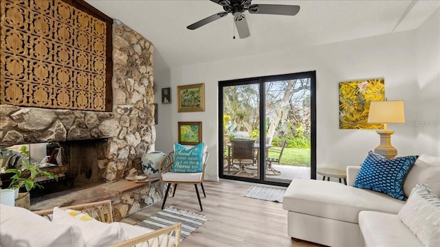 living room with lofted ceiling, a stone fireplace, and light hardwood / wood-style floors