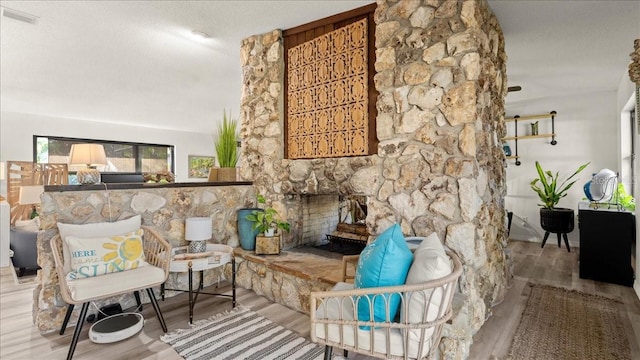 sitting room featuring hardwood / wood-style flooring, a stone fireplace, and a textured ceiling