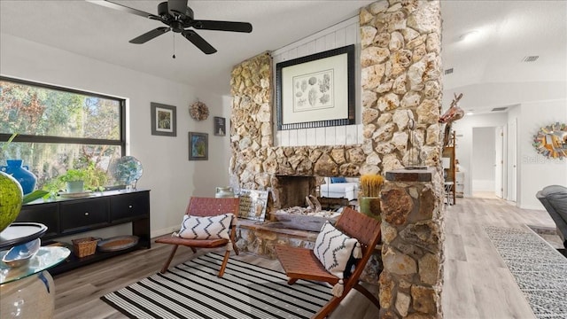 living area featuring a fireplace, ceiling fan, and light wood-type flooring