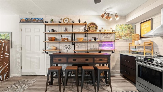 kitchen featuring wood-type flooring, wall chimney range hood, a textured ceiling, and electric stove