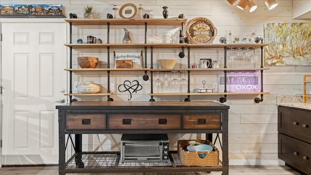 bar featuring dark brown cabinetry, wood-type flooring, and light stone countertops