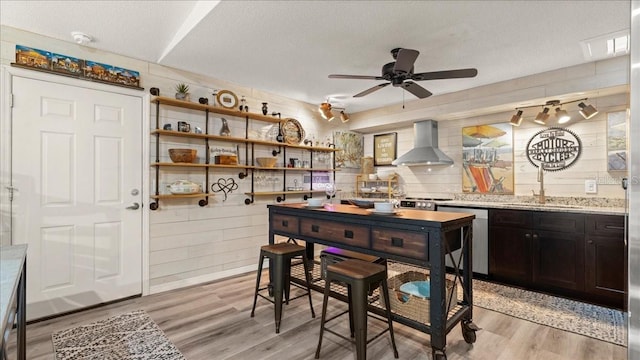 kitchen with sink, stainless steel dishwasher, wall chimney range hood, a textured ceiling, and light hardwood / wood-style flooring