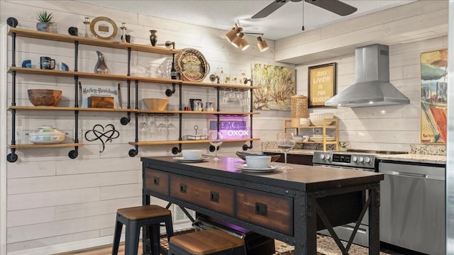 kitchen with ceiling fan, appliances with stainless steel finishes, a kitchen bar, and wall chimney exhaust hood