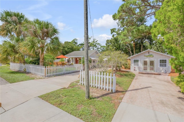 view of front of home with driveway, a fenced front yard, an outbuilding, and french doors