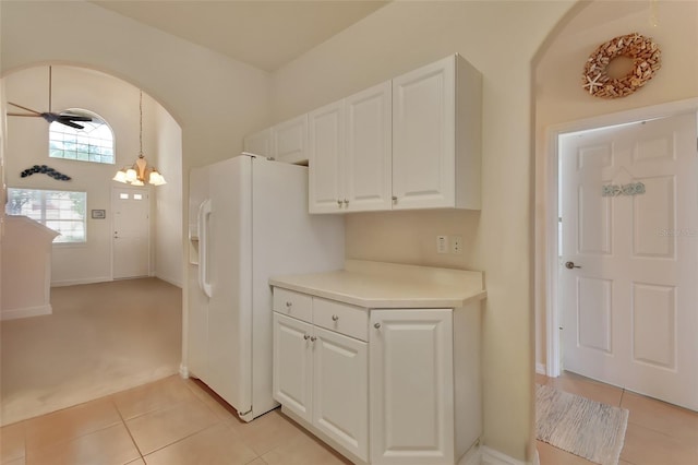 kitchen with light tile patterned flooring, pendant lighting, ceiling fan with notable chandelier, white cabinets, and white refrigerator with ice dispenser