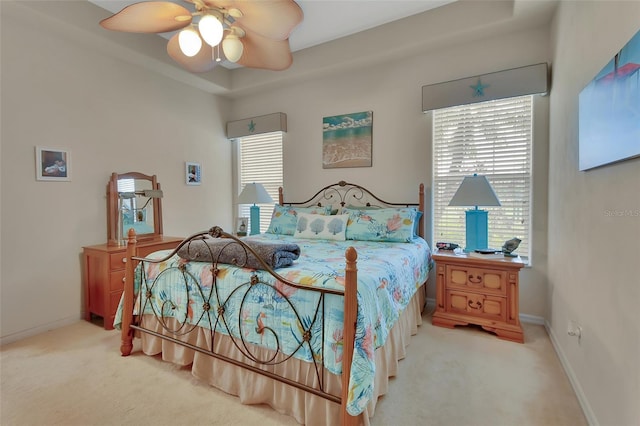 bedroom featuring ceiling fan, a tray ceiling, carpet flooring, and multiple windows