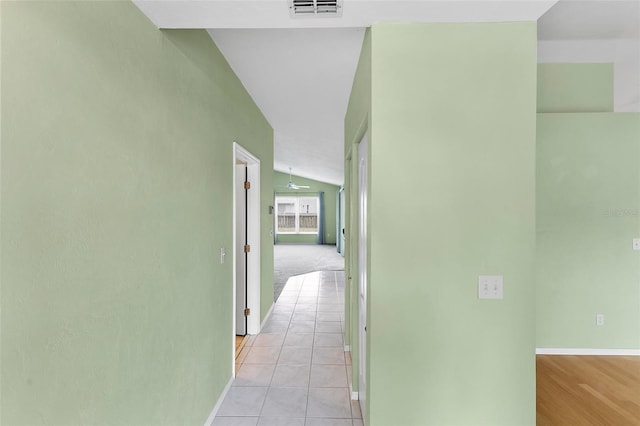 hall featuring vaulted ceiling, light tile patterned flooring, visible vents, and baseboards