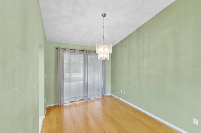 unfurnished room featuring a chandelier, wood finished floors, and baseboards