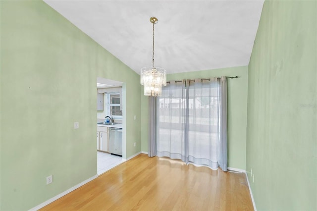 unfurnished dining area with light wood-style floors, a sink, vaulted ceiling, a chandelier, and baseboards