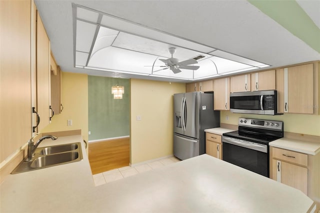 kitchen featuring light countertops, appliances with stainless steel finishes, light brown cabinets, a sink, and ceiling fan