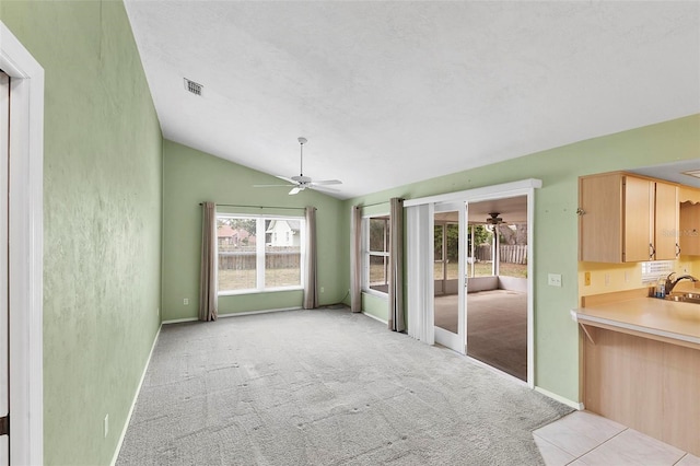 unfurnished dining area with light carpet, a sink, visible vents, a ceiling fan, and vaulted ceiling