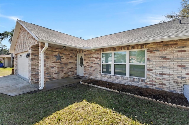 property entrance with an attached garage, a shingled roof, a lawn, and brick siding