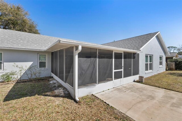 rear view of property with a sunroom, roof with shingles, a lawn, stucco siding, and a patio area