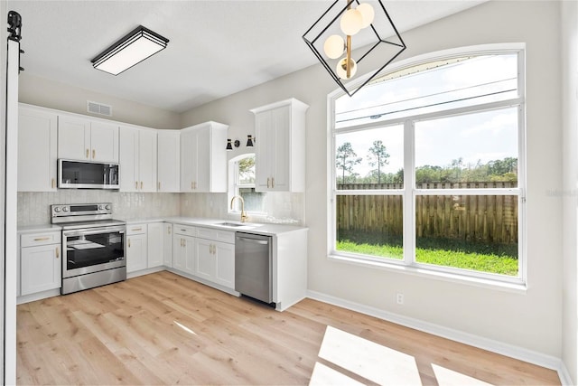 kitchen with sink, backsplash, pendant lighting, stainless steel appliances, and white cabinets