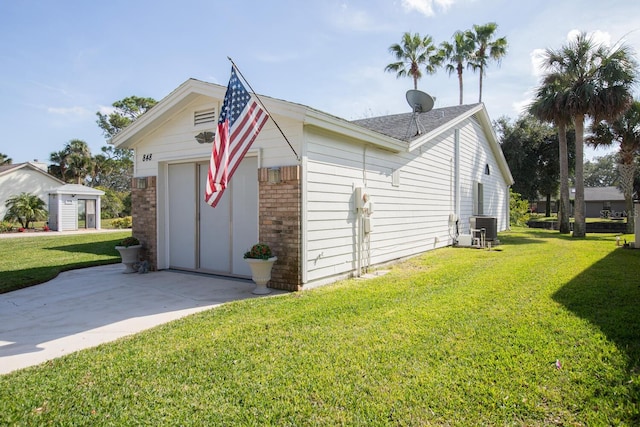 view of side of property featuring a lawn, central AC, concrete driveway, a garage, and brick siding