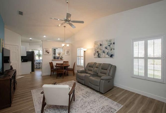 living room with ceiling fan with notable chandelier, hardwood / wood-style floors, and high vaulted ceiling