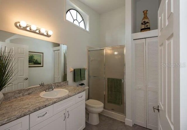 bathroom with a high ceiling, vanity, a shower with shower door, and toilet