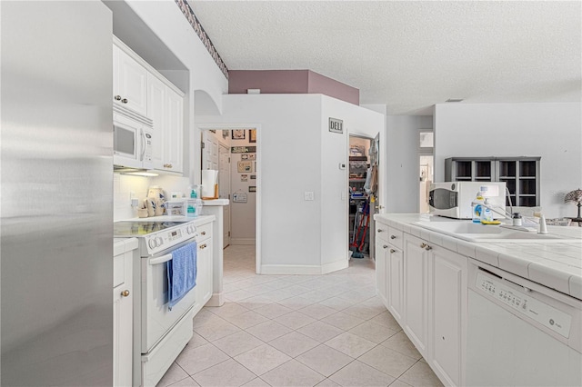 kitchen featuring light tile patterned flooring, a textured ceiling, tile counters, white appliances, and white cabinets