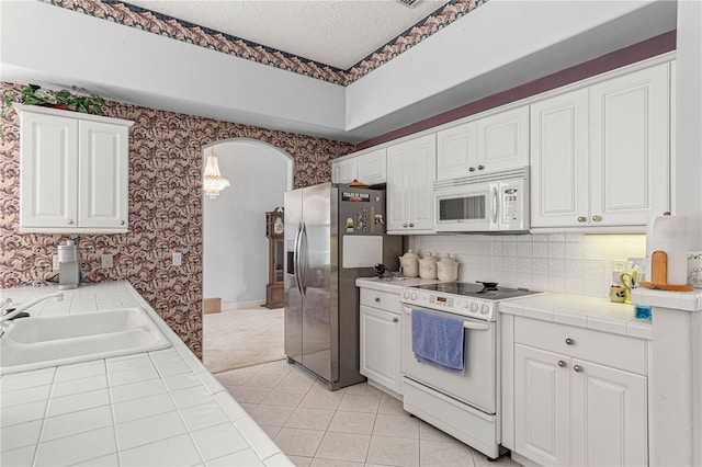 kitchen with sink, tile counters, white cabinets, and white appliances