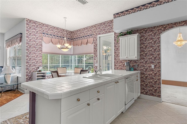 kitchen featuring sink, hanging light fixtures, white dishwasher, white cabinets, and tile countertops