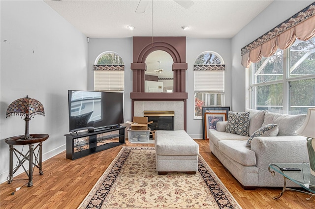 living room with hardwood / wood-style floors, a tile fireplace, a textured ceiling, and ceiling fan