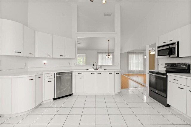 kitchen featuring sink, white cabinetry, hanging light fixtures, stainless steel appliances, and a high ceiling