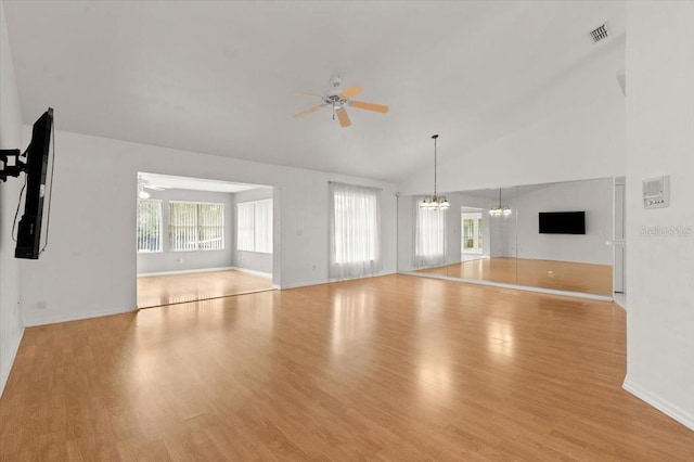 unfurnished living room with ceiling fan with notable chandelier, high vaulted ceiling, plenty of natural light, and light hardwood / wood-style floors