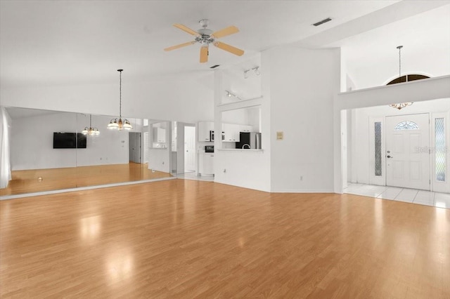 unfurnished living room with ceiling fan with notable chandelier, high vaulted ceiling, and light wood-type flooring