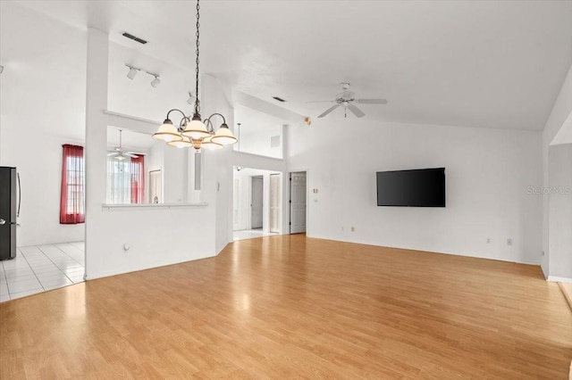 unfurnished living room with high vaulted ceiling, ceiling fan with notable chandelier, and light wood-type flooring