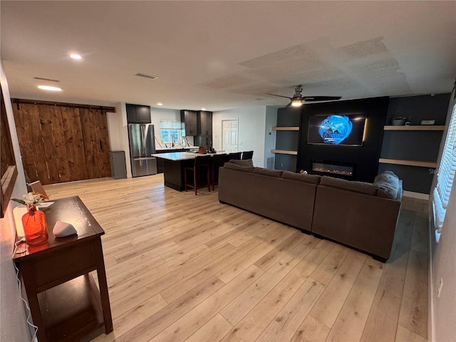 living area featuring visible vents, a glass covered fireplace, ceiling fan, light wood-style floors, and recessed lighting