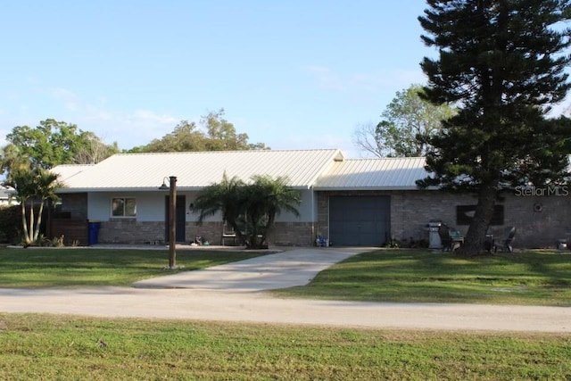 ranch-style home featuring a front yard, metal roof, driveway, and an attached garage