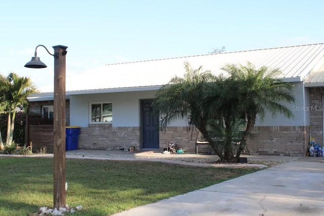 ranch-style home with a front yard, brick siding, metal roof, and stucco siding