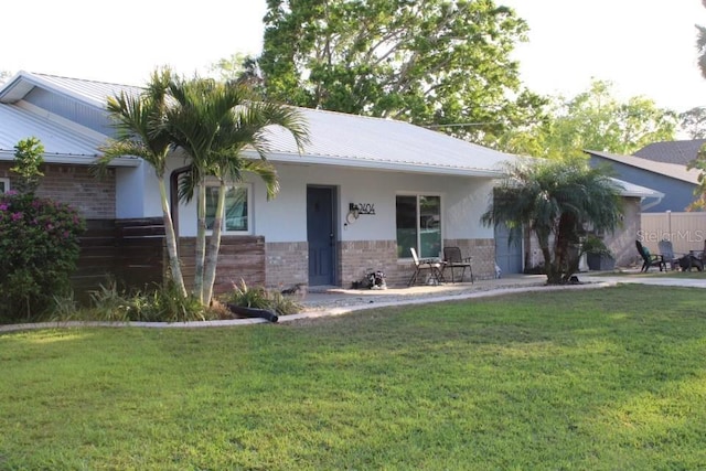 ranch-style house featuring a front yard, brick siding, metal roof, and stucco siding